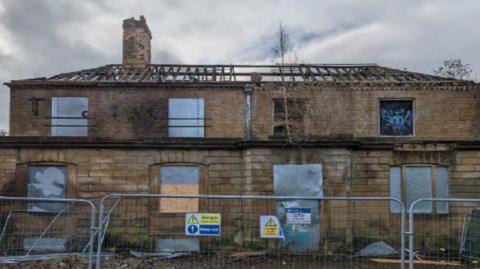 A derelict house behind metal fencing