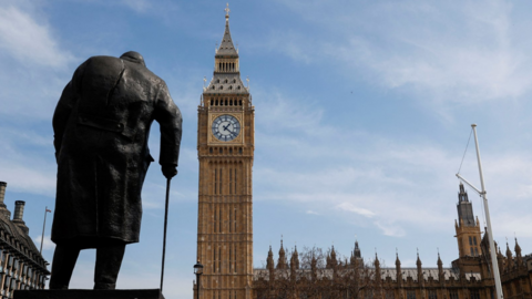 The back of the bronze statue of Churchill leaning on a walking stick, with Big Ben and parliament in the background