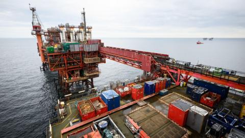 A drilling platform for oil in the North Sea The view is diagonal. A boat can be seen in the distance behind it.

