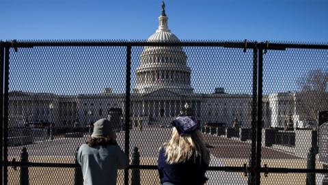 People view the U.S. Capitol, behind security fencing