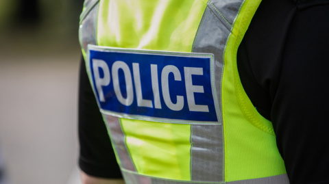 Back of a police officer's uniform - showing a green vest with police on the back