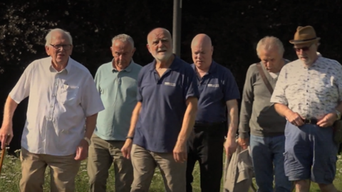 Six men in trousers and shirts aged between 60 and 70 on a walking outing.