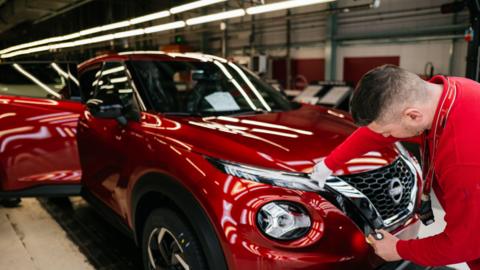 An employee, wearing a red shirt, inspects a red sports utility vehicle on the production line with Nissan Juke and Nissan Qashqai at the Nissan factory in Sunderland, UK, on Friday, 24 November, 2023.