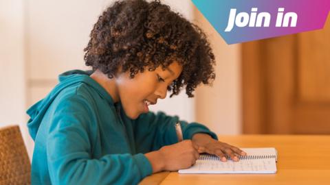 Boy sits at a table and writes in a notebook. 