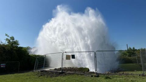 A burst water pipe on a field sends huge burst of water into the air 