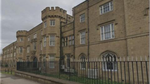 A stone built building has two large turrets, black railings and many large windows