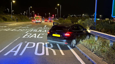 A black car crashed into a roadside barrier at the side of the road at night.