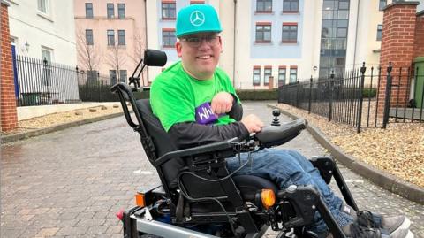 Adam sat in a wheelchair with a green hat