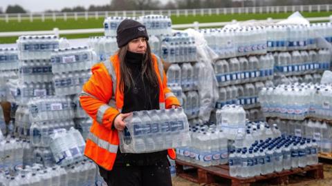 A woman loads bottled water at an emergency water distribution point