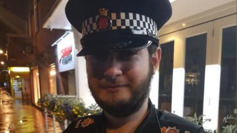 A close-up image of William Towner in uniform, wearing a peaked cap, standing in a lit street at night with buildings behind.