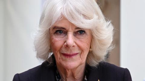 Queen Camilla looks away from camera while wearing a black suit jacket, pictured in London in February.