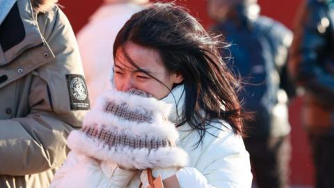 A woman wearing a white winter coat, her hair blowing in the wind