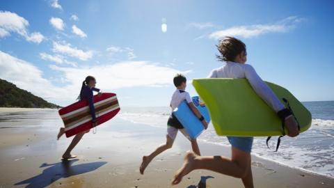 Children running along the beach with surf boards