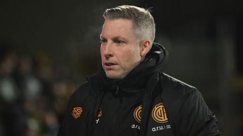 Cambridge United manager Neil Harris walking forward wearing black club winter jacket