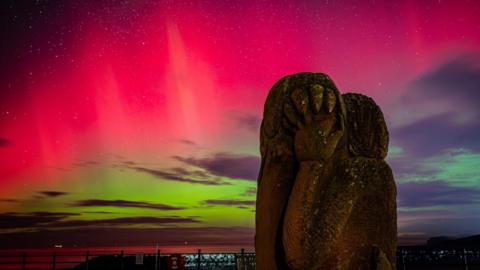 A rocky sculpture stands in front of a red and green sky.