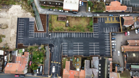 An aerial view of a car park with 100 spaces, flanked by houses.