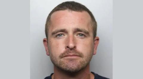 Police mugshot of Simon Orr, who is facing the camera and wearing a dark-coloured top