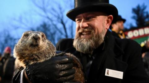 Man in black jacket and top hat holding a gopher