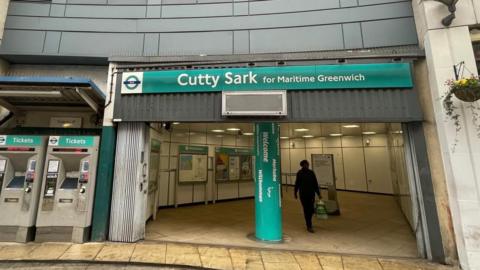 Front entrance of Cutty Sark station in Greenwich. The picture shows two ticket mchines and the entrance hall during daylight, with one person walking in