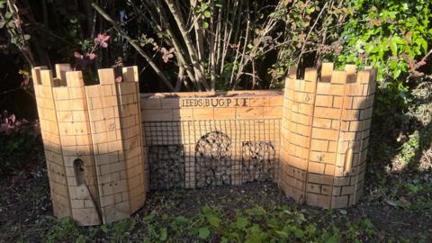A wooden model of a bear pit with words on the front reading 'Leeds Bug Pit'.