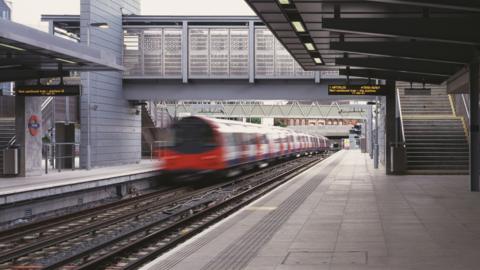Platform at Stratford station shows departing Jubilee line train on left with bridge ahead and steps to the right. A departure board shows Waterloo