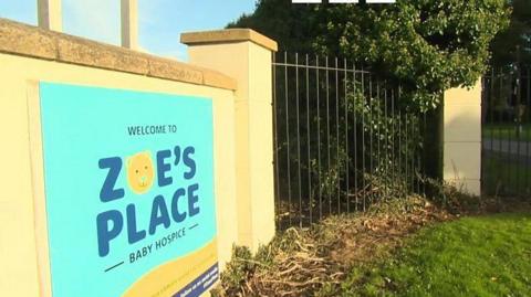 The Zoe's Place logo, which feature's blue letters and a teddy bear's face, on the yellow brick wall outside its Liverpool hospice