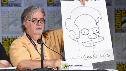 Matt Groening at the 2017 Comic-Con in San Diego, holding up a picture of Apu