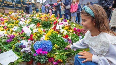 A girl leaves flowers at Hillsborough Castle, south of Belfast in Northern Ireland on September 11, 2022, following the death of Britain's Queen Elizabeth II