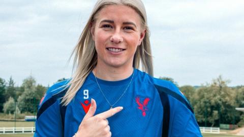 Bethany England points to the Crystal Palace crest on a blue training top