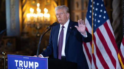 Donald Trump stands at a lecturn in front of two US flags as he speaks to members of the media during a press conference at his Mar-a-Lago Club in Florida 