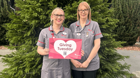 Two nurses holding a card that says giving Tuesday on it