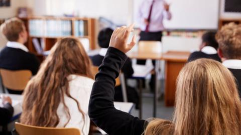 A class of school pupils. A female pupil has her hand raised.