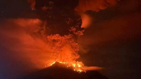 Volcano with lava flowing down it and smoke in the air