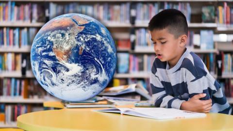 A boy reads a book in the library. Superimposed next to him is the world