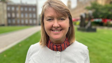 Sarah Gibson smiling at the camera in front of the Houses of Parliament in Westminster
