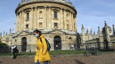 Woman wears mask walking past Radcliffe Camera