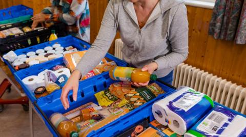 A volunteer sorts food and household supplies into crates at a food bank
