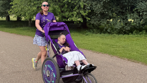 Woman with brown hair running with her daughter who is sat inside a wheelchair