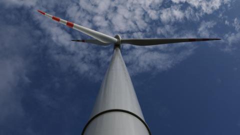 A wind turbine tower and blades viewed from the ground looking up into a blue sky with light clouds