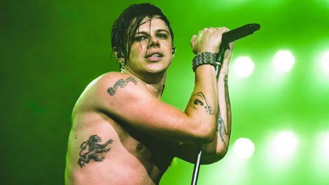 Yungblood topless on stage with a microphone with a green background