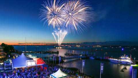 View of crowds watching fireworks from the shore with a dark blue sky