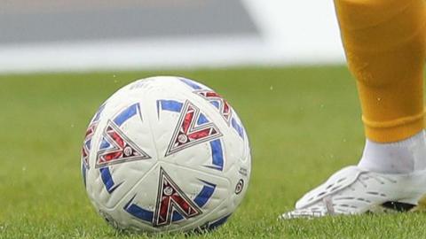A National League matchball about to be kicked by a white boot and yellow sock