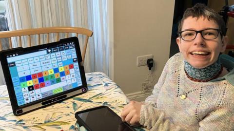 Beth Moulam sitting at a table on which is place her assisted technology screen.