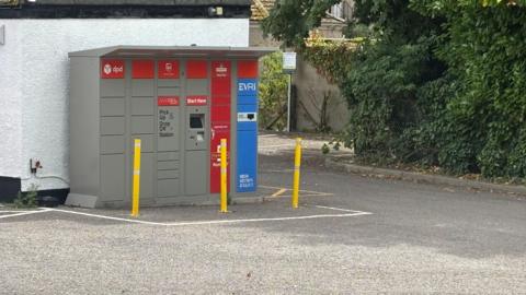 A locker for parcels is pictured in a car park.