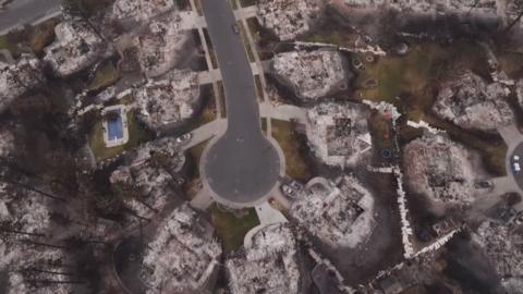 The aerial still shows homes destroyed down to their foundations, with burned cars still parked in some driveways.
