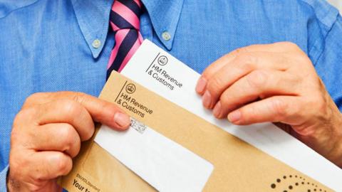 A man's hands hold an HMRC tax envelope 