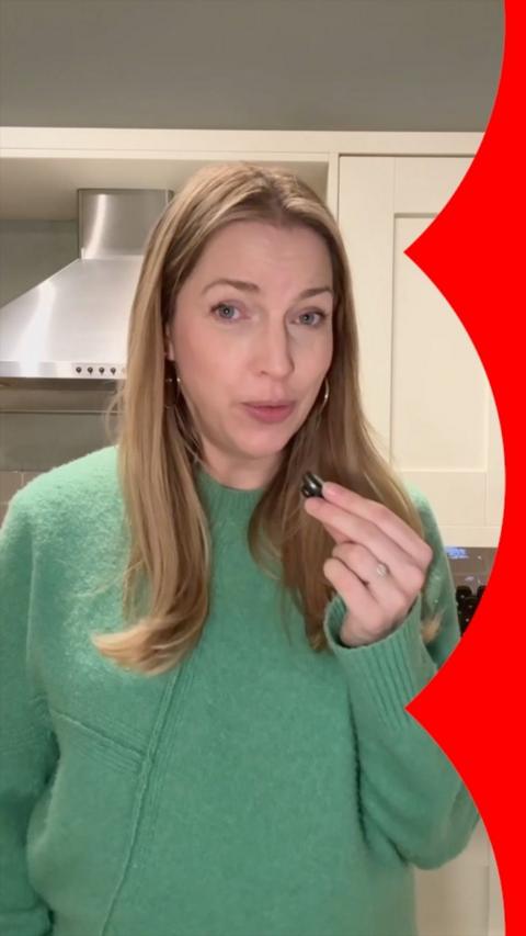 A woman in a green jumper stands in a kitchen