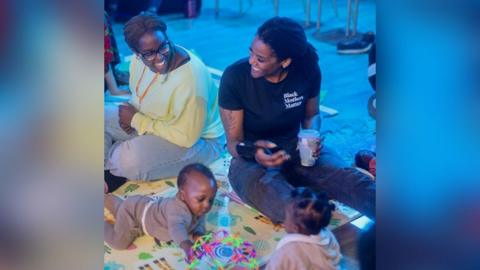 Two women sitting with two babies on a blanket