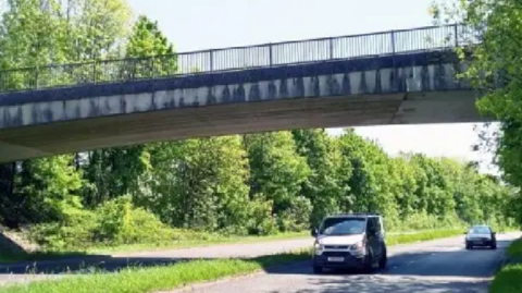 A van and a car travelling under the one of the bridges on the A591. The L-shaped joints can be seen on the bridge.