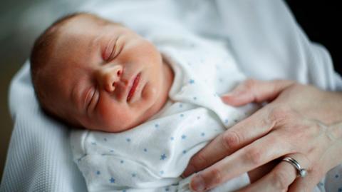 A baby sleeping in its mother's arms looking rested and content